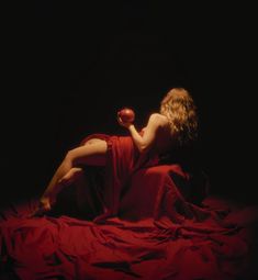 a woman in a red dress sitting on a bed with an apple next to her