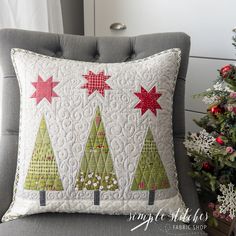 a christmas tree pillow sitting on top of a gray chair next to a christmas tree