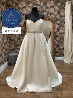 a white wedding dress on display in front of a floral wallpapered background with the bridal wn5d logo