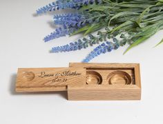 two wedding rings in a wooden box next to lavender flowers and greenery on a white surface