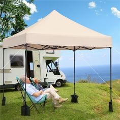 two men sitting in lawn chairs under a tent next to an rv on the grass