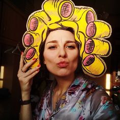 a woman wearing a yellow hat with pink flowers on it's head and holding her hand up to her face