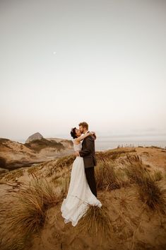 a bride and groom kissing in the sand dunes on their wedding day at sunset or sunrise