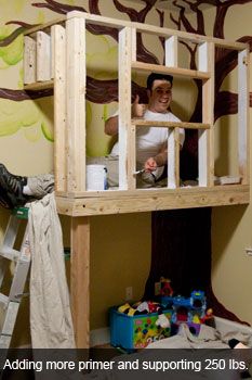 a man standing on top of a wooden bunk bed next to a tree wall mural