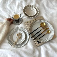 a table set with plates, spoons and utensils on top of a white sheet