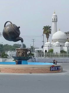 a large metal teapot sitting on top of a fountain in front of a white building