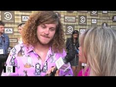 a man with long hair talking to someone on the red carpet at an awards event