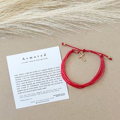 a red string bracelet with a cross on it and a card attached to the cord