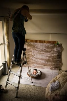 a woman standing on top of a ladder next to a baby in a diaper