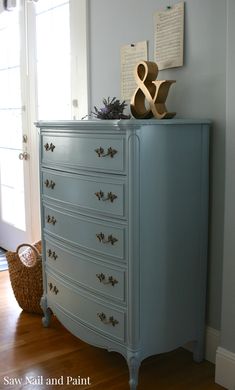 an old dresser painted blue with gold handles and knobs on the top, next to a wicker basket