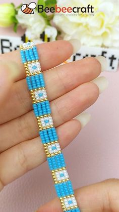 a hand holding a blue and white beaded bracelet on it's fingers with flowers in the background