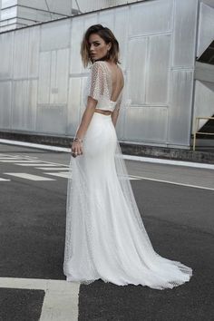 a woman in a white wedding dress standing on the street with her back to the camera