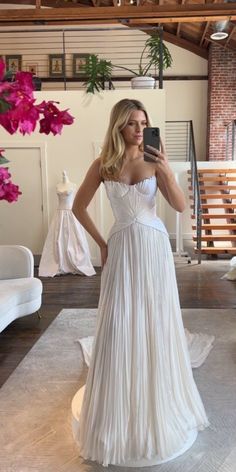 a woman in a white dress taking a selfie with her cell phone while standing on the floor