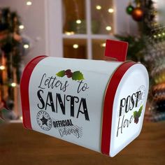 a red and white mailbox sitting on top of a wooden table next to a christmas tree