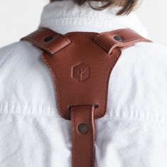 the back of a person wearing a white shirt and brown leather suspenders with buttons