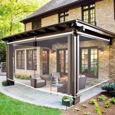 a covered patio with chairs and tables in front of a brick house