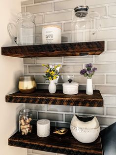 three wooden shelves with jars and vases on them in a kitchen area next to a white brick wall