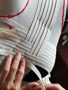 a woman is working on a piece of white fabric with red string and beading