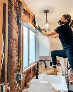 a woman in a black shirt and mask working on a kitchen wall with exposed wood