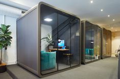 an office cubicle with glass walls and blue chairs in the corner, next to a potted plant