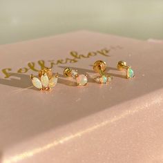 three pairs of opalite studs sitting on top of a pink box with gold lettering