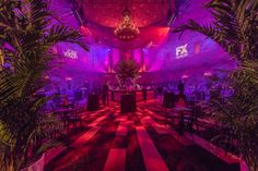 an indoor event with purple lighting and palm trees in the center, surrounded by black and white checkered flooring