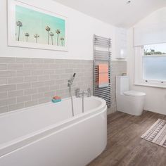 a bathroom with a bathtub, toilet and rugs on the wood flooring