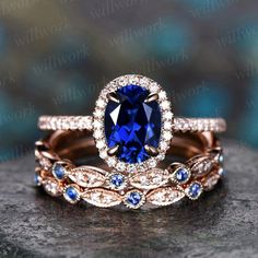 two wedding rings with an oval blue sapphire surrounded by smaller blue and white diamonds, on top of a rock