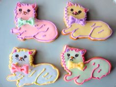 four decorated cookies on a plate with one cat and the other kitten wearing a bow tie