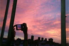 a person taking a photo with their cell phone in front of a window at sunset