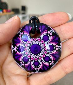 a hand holding a purple and pink flower design glass pendant on a black cord necklace