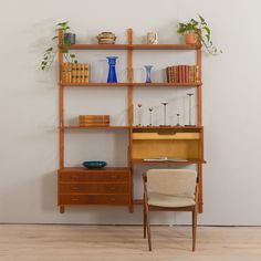 a wooden shelf with books, vases and other items on it next to a chair