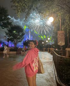 a woman is walking down the street with fireworks in the background