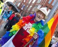 a man in a white hat is holding a rainbow flag and smiling at the camera