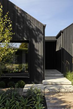 the house is black and has large windows on it's sides, along with wooden steps that lead up to the front door