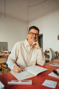 a man sitting at a desk in front of a laptop computer smiling and holding his hand to his chin