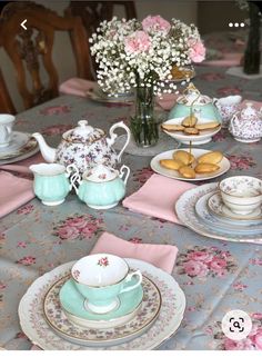 the table is set with tea cups, plates and flowers in vases on it