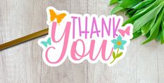 a thank you sticker sitting on top of a wooden table next to green leaves