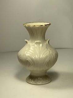 a white vase sitting on top of a table next to a light colored wall behind it