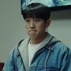 a young man in a denim jacket standing next to a tv screen with an angry look on his face