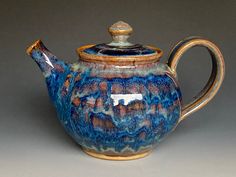 a ceramic teapot with a wooden handle on a gray background, decorated with blue and brown swirls