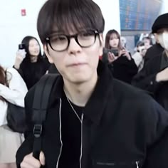 a man wearing glasses and a black jacket is standing in front of a group of people