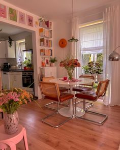 a dining room table and chairs with flowers in vases on the end tables next to each other