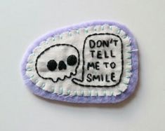 a purple and white patch with a skull saying don't tell me to smile