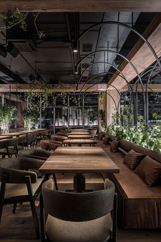 an empty restaurant with wooden tables and brown chairs, plants growing on the wall behind them