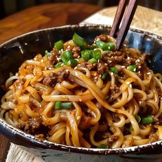 a close up of a bowl of noodles with meat and green onions on the side