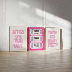 three pink and white posters with words on them sitting in front of a wooden floor