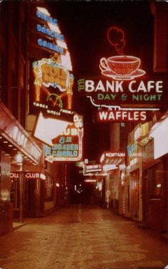 an old photo of a city street at night with neon signs and coffee cups on the buildings