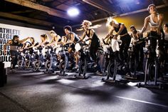 a group of people riding bikes on top of a floor next to each other in front of a sign