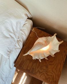 a wooden table with a lamp on top of it next to a white bed and pillows